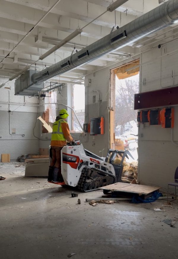 Demolition worker operating skid steer in interior space for commercial or residential rebuild.