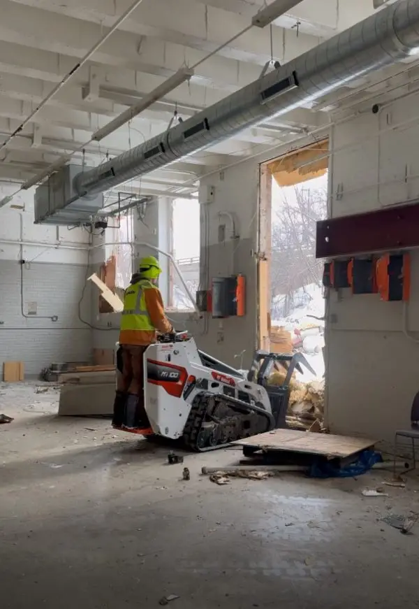 Demolition worker operating skid steer in interior demolition project.