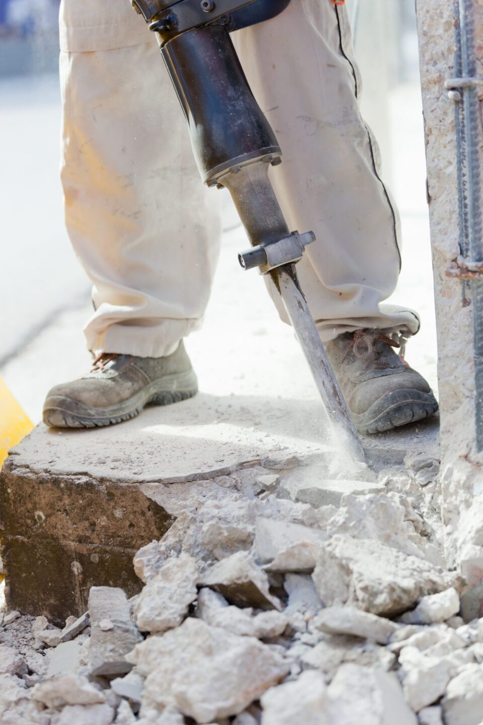 Construction worker using jackhammer to break concrete for foundation work.
