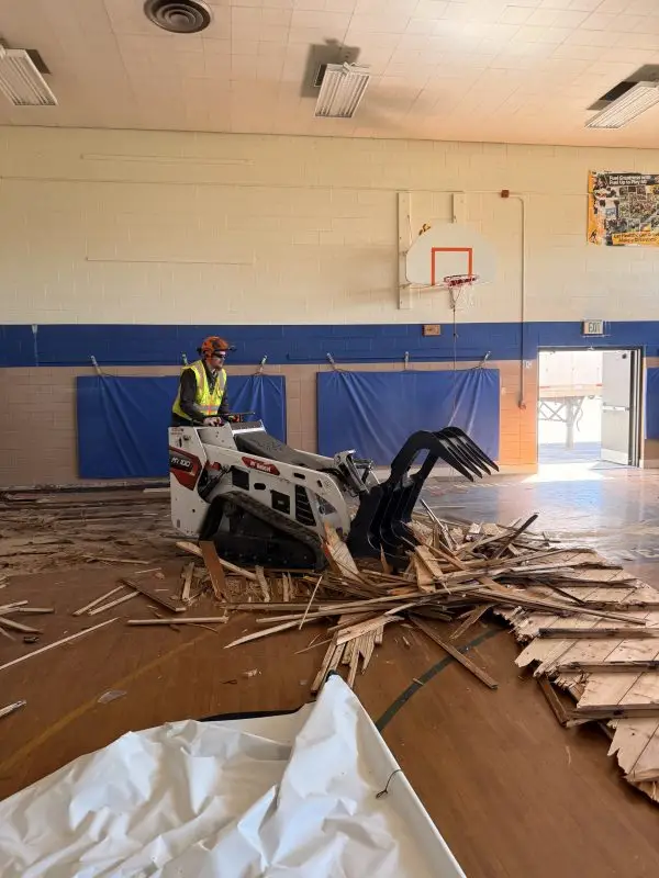 Selective demolition in progress at school gym, HammerCore Group equipment and debris.
