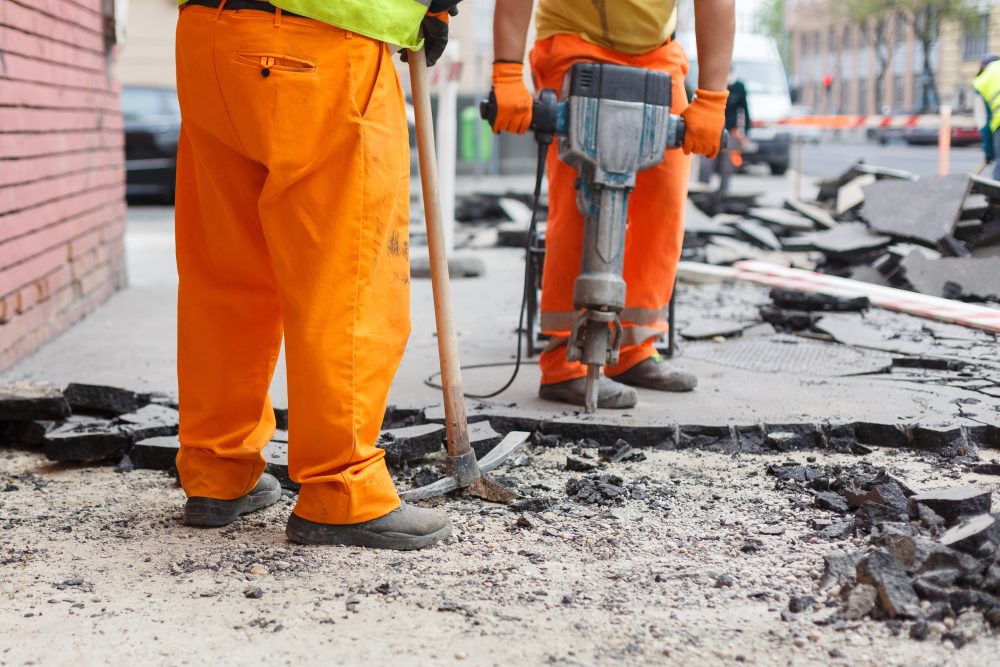 Construction worker repairing asphalt road in Iowa, demolition and construction services.