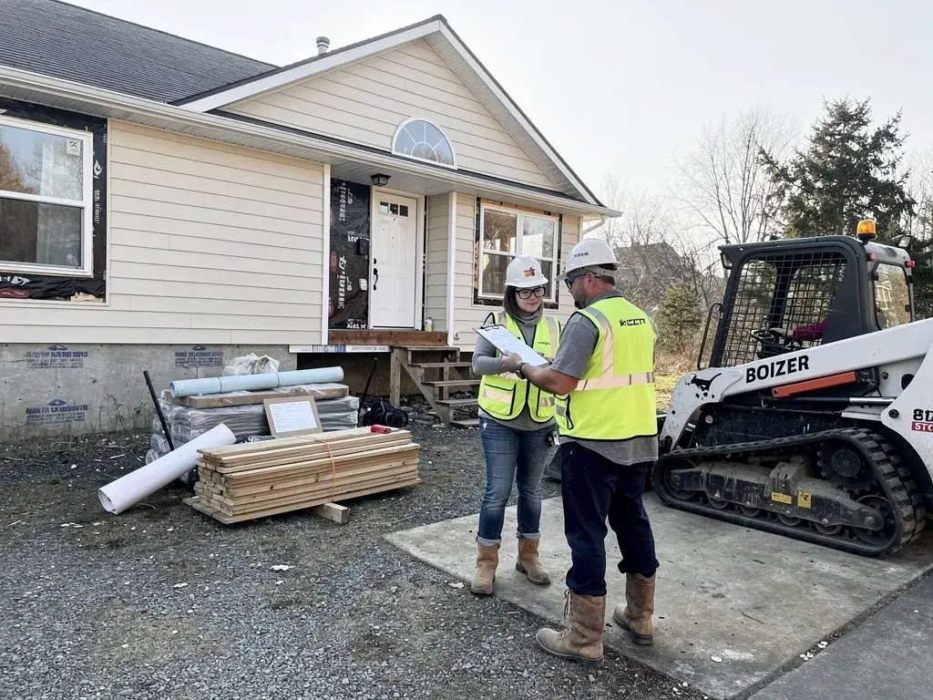 HammerCore Group demolition contractors reviewing plans near residential structure and Bobcat equipment.