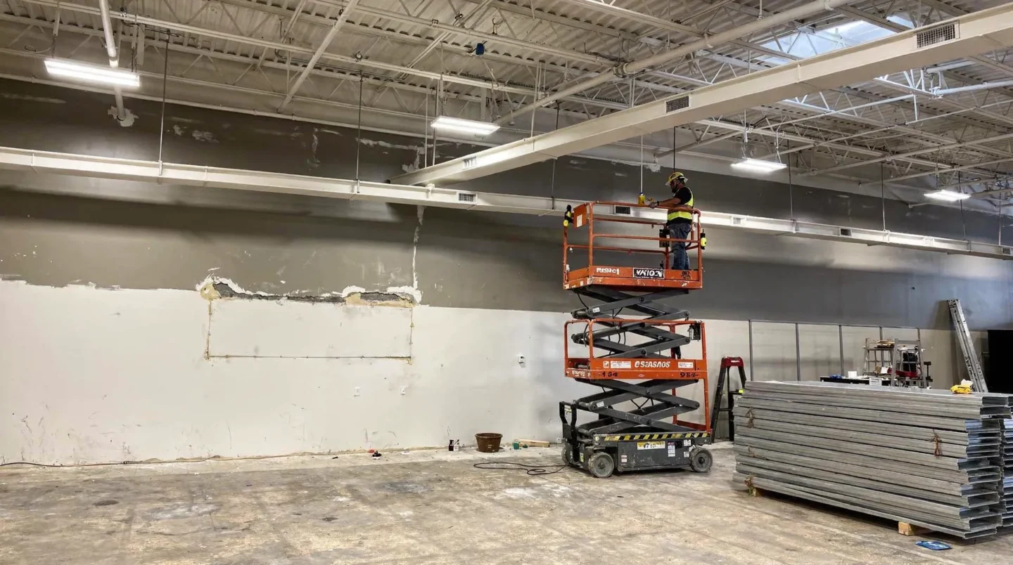 Worker on scissor lift repairing building exterior, gutter installation preparation.