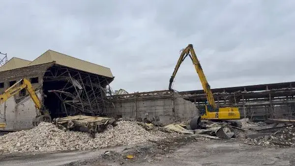 Demolition machinery dismantling an industrial building amid debris.