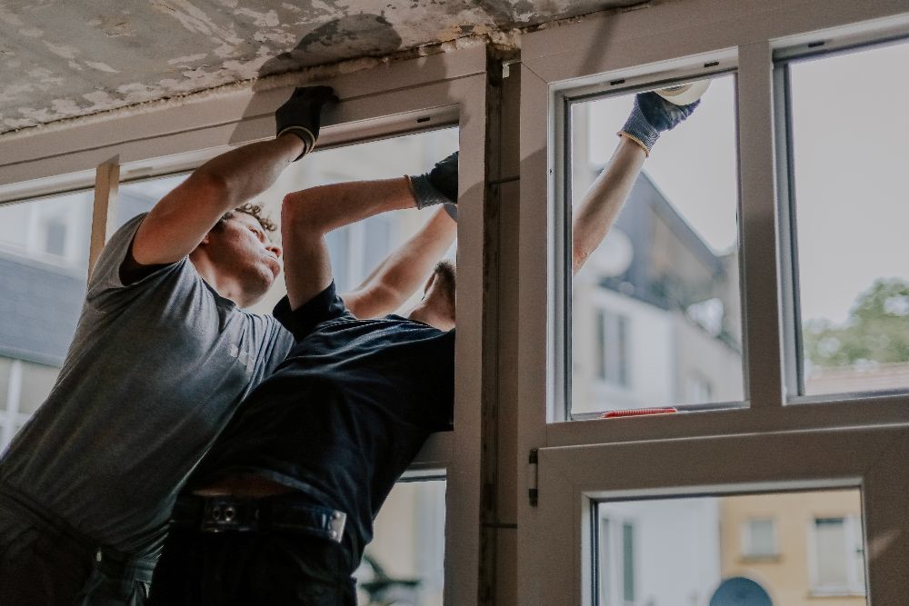 Two installers fitting a new replacement window into the frame of a home
